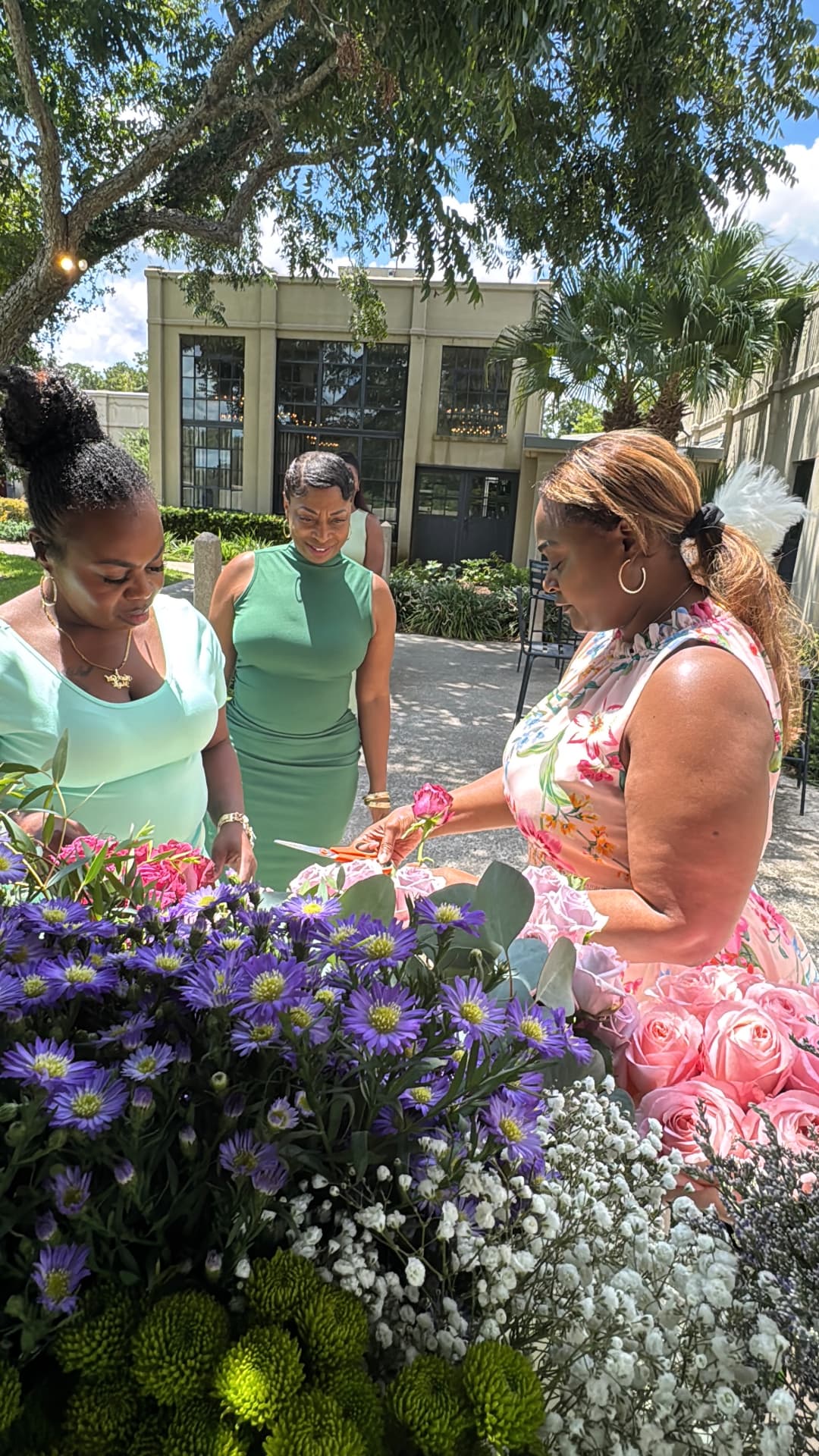 Guests trimming pink roses at a lush garden flower bar during a Buzz & Blossoms brunch