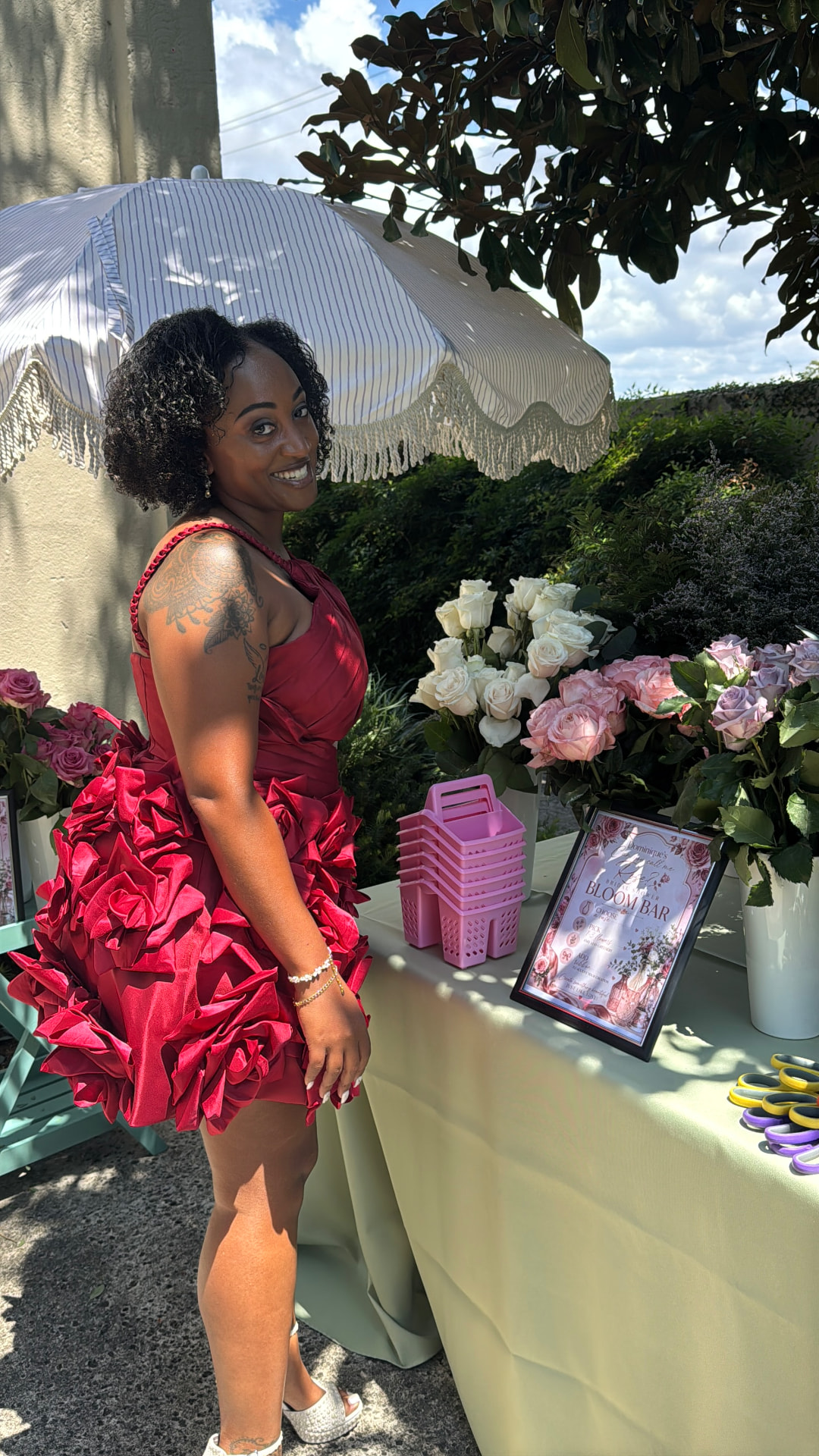 The bride in a burgundy rose dress beside the Bloom Bar at her bridal shower