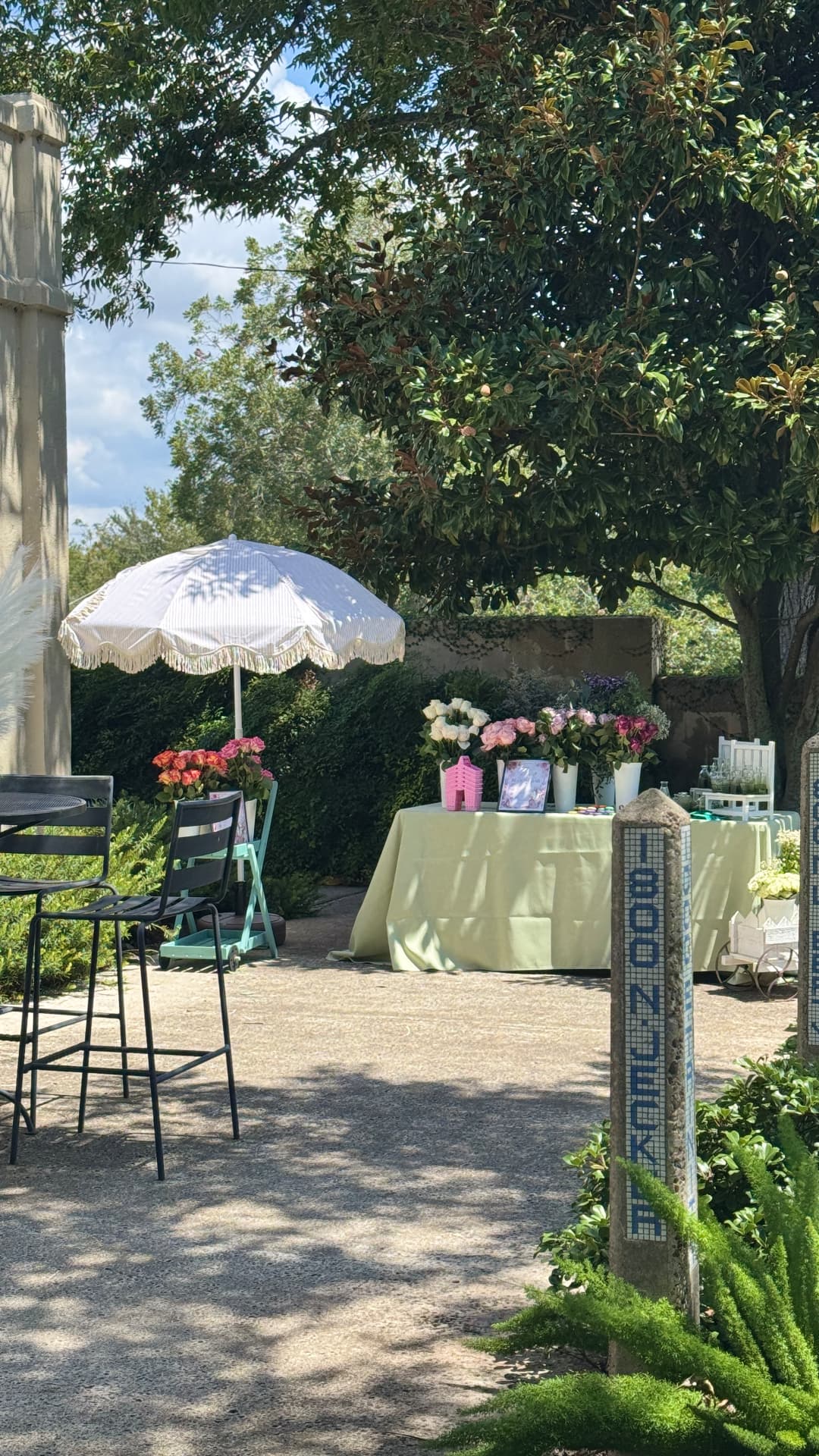 Garden patio bloom bar under a fringed umbrella with buckets of roses and greenery